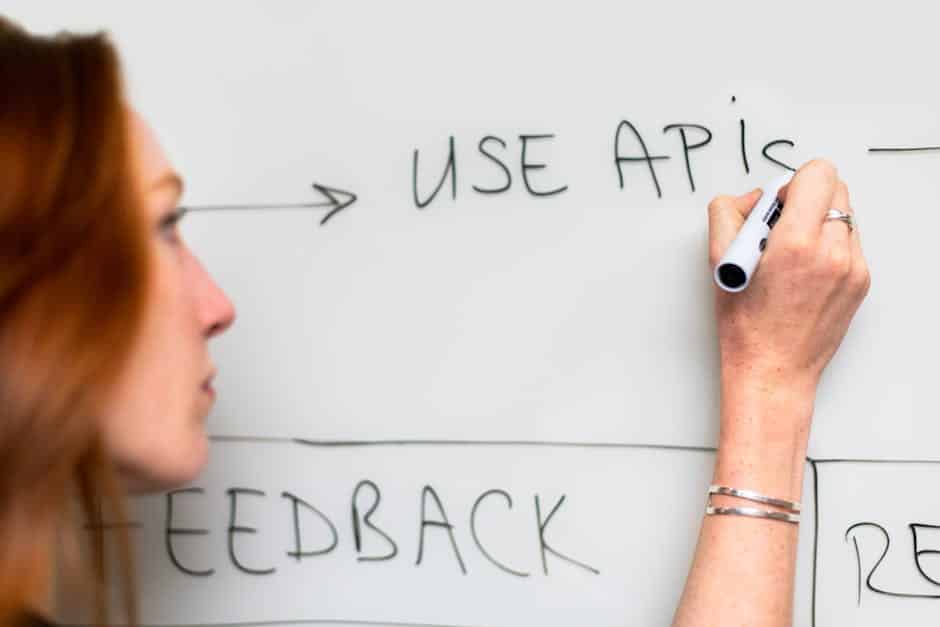 API design best practices - A woman writes 'Use APIs' on a whiteboard, focusing on software planning and strategy.