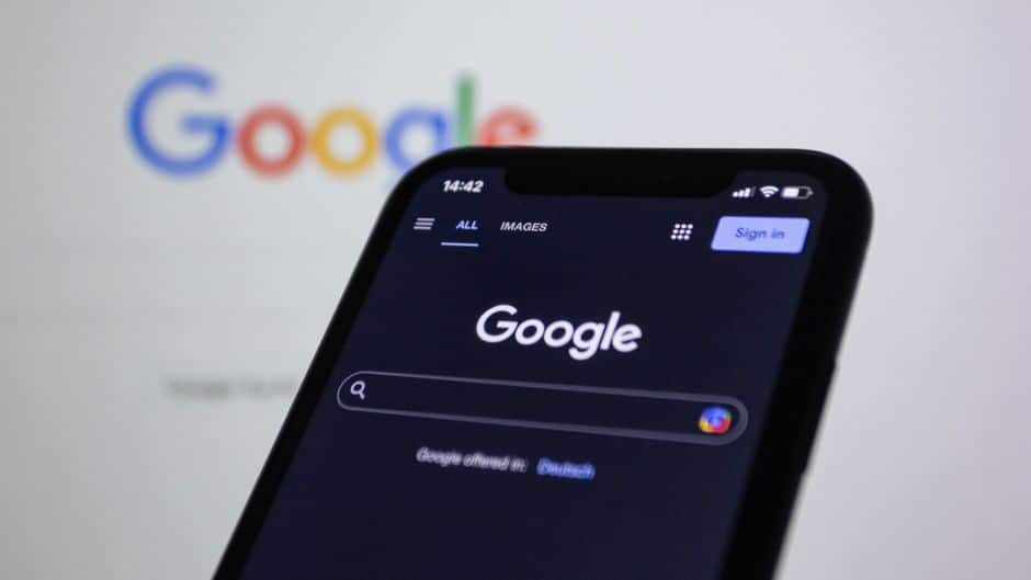 web development news - Smartphone screen showing Google search in dark mode with the Google logo in the background.